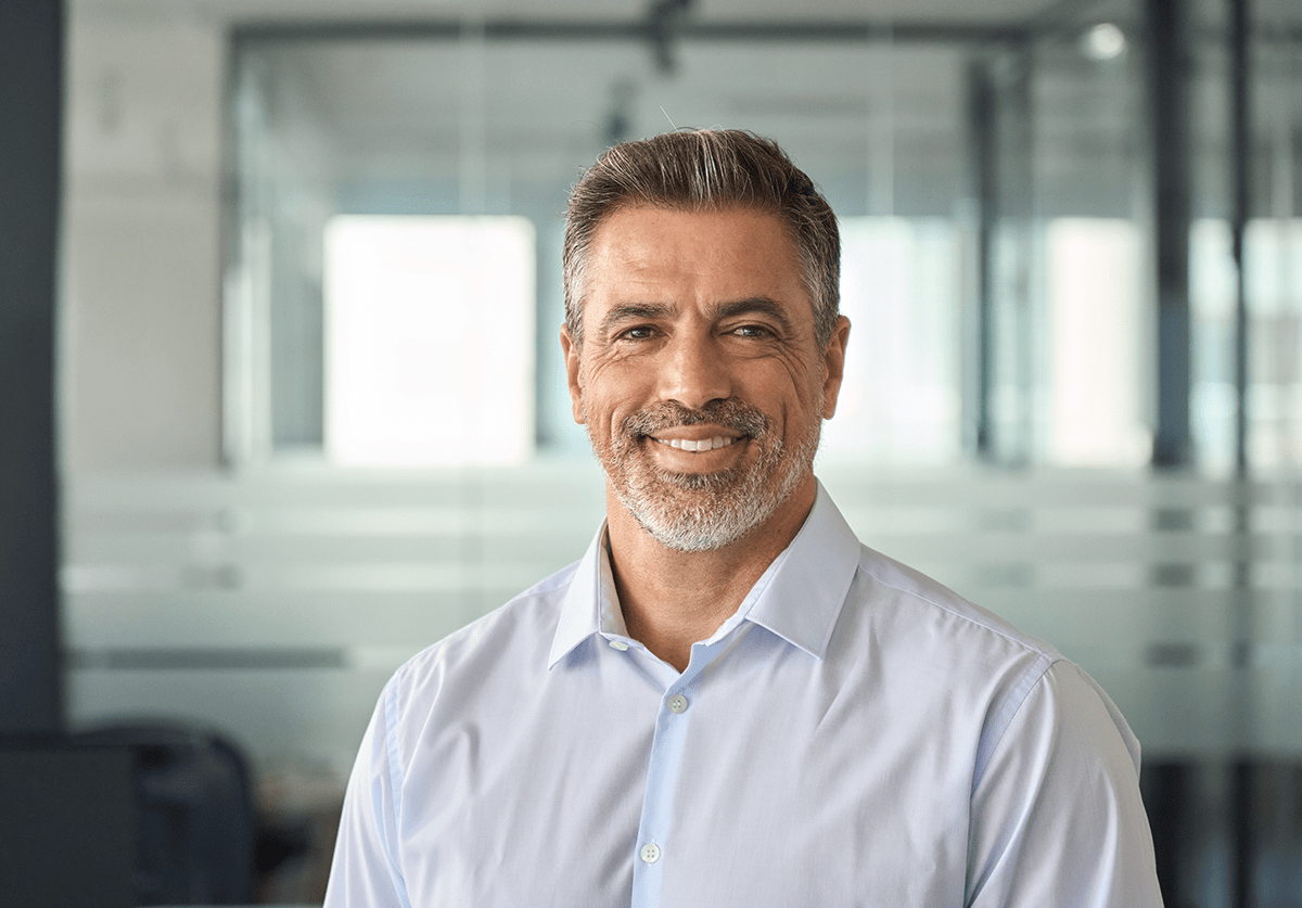 Smiling professional man in a light blue shirt standing in a modern office environment.