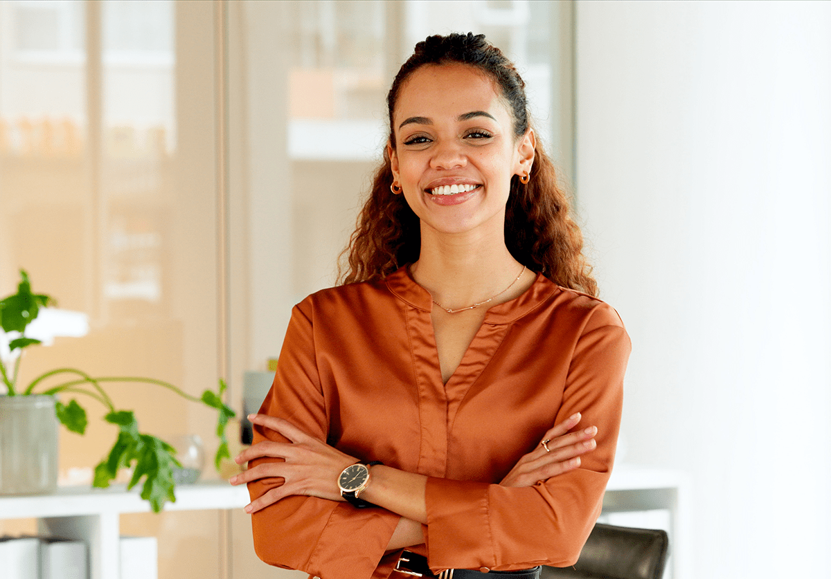 Smiling professional woman standing confidently with arms crossed in a modern office setting.